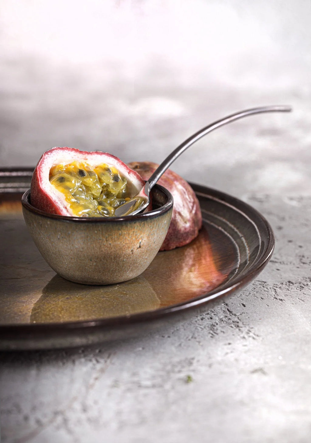 Assiette en grès émaillé brun gris moucheté avec fruit de la passion coupé