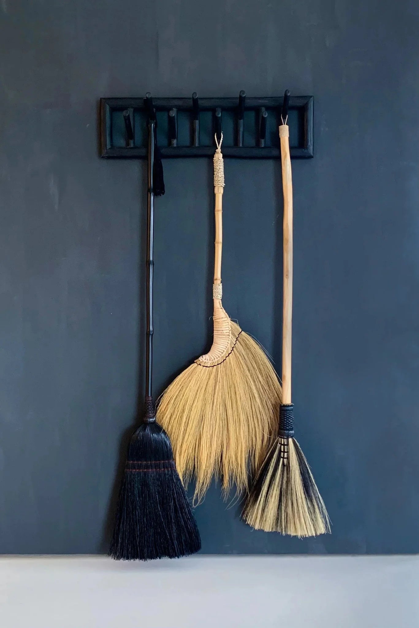 Trois balais rustiques en fibres naturelles et bambou beige doré accrochés à un support mural noir
