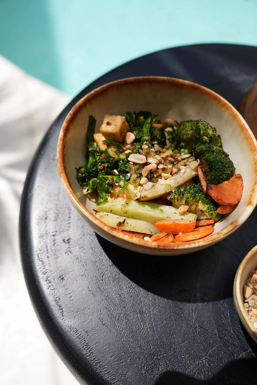 Bol en céramique artisanale beige avec légumes rôtis, tofu et noix