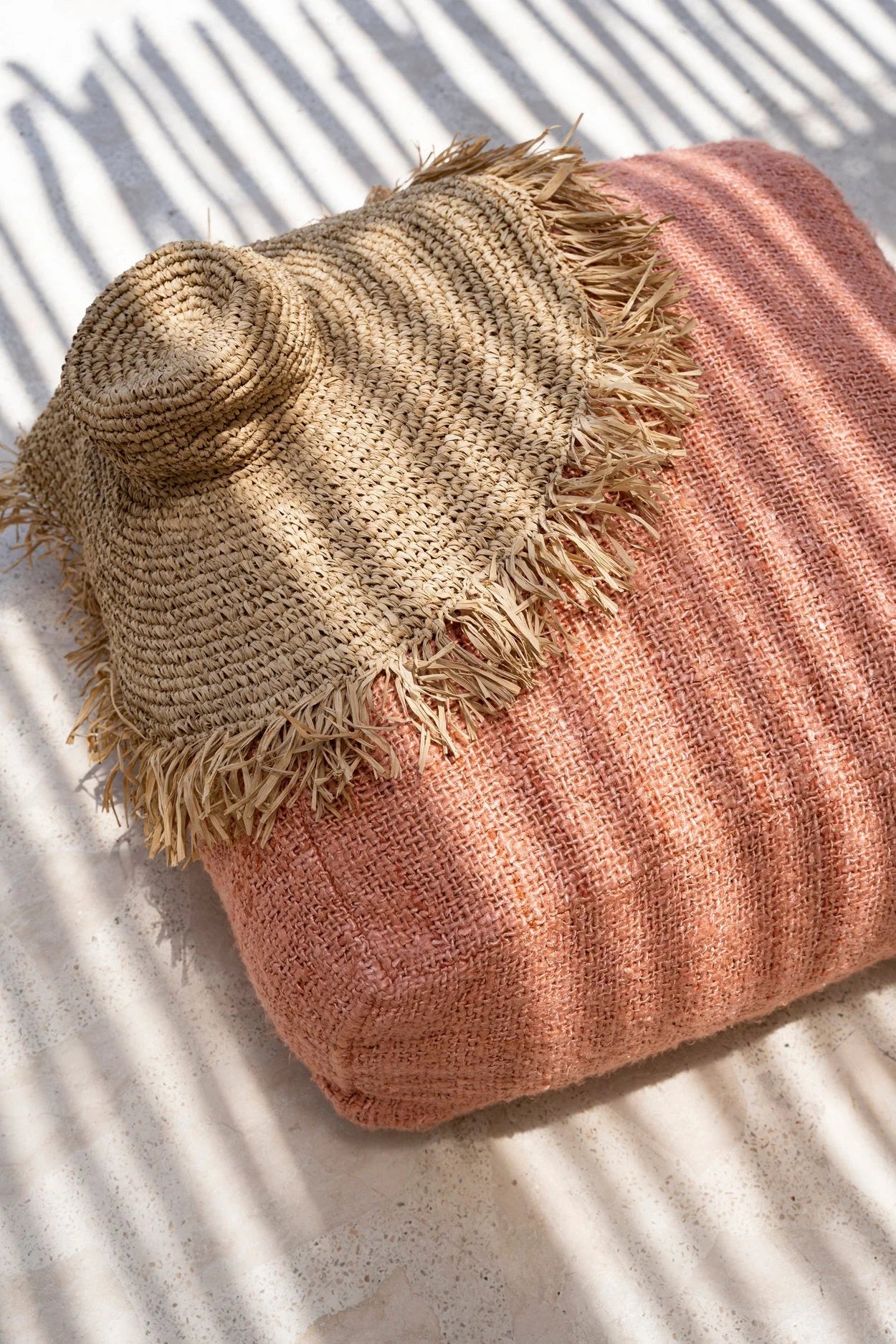 Chapeau à large bord en raphia tressé frangé sur coussin rose poudré texturé