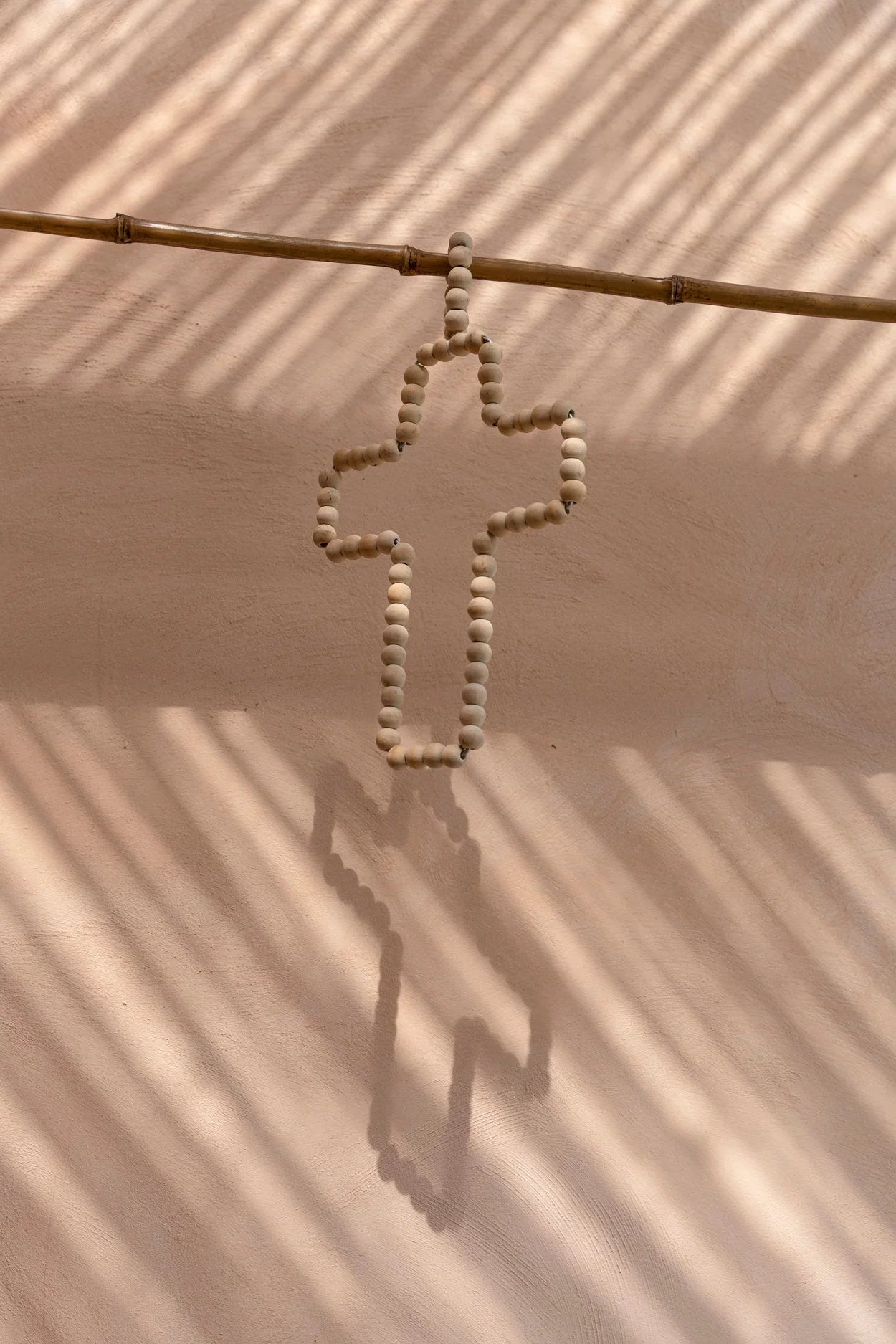 Croix murale en perles de bois naturel beige suspendue à une tige de bambou
