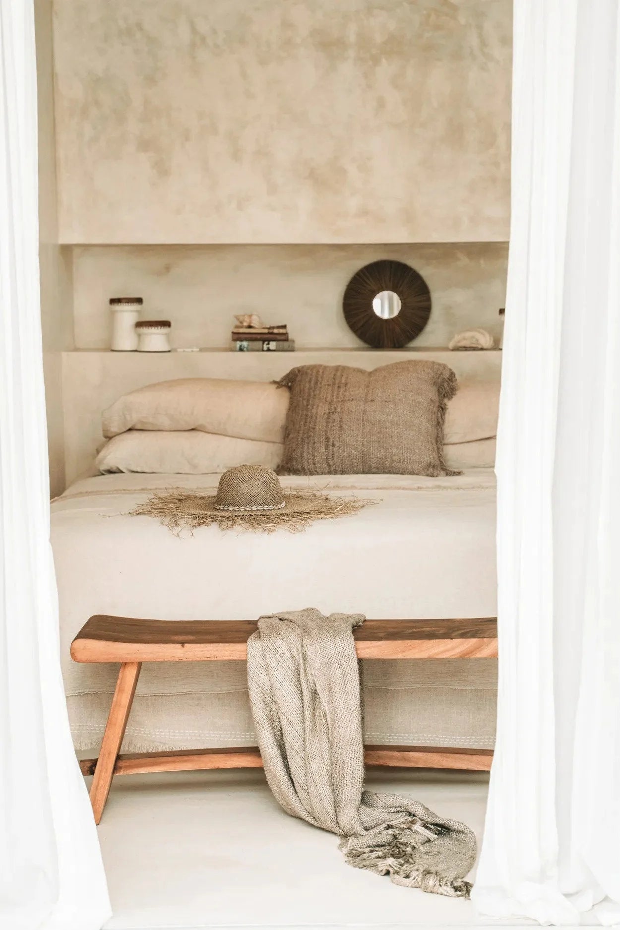 Housse de coussin coton beige avec franges dans une chambre neutre avec étagère et banc