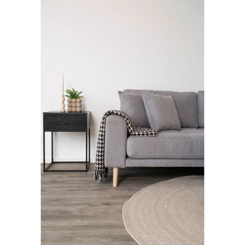 Canapé gris capitonné, pieds bois, plaid pied-de-poule noir et beige à franges sur accoudoir