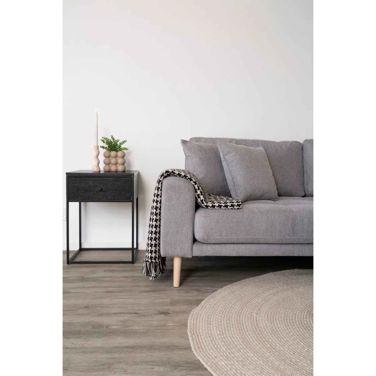 Canapé gris capitonné, pieds bois, plaid pied-de-poule noir et beige à franges sur accoudoir