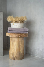 Panier tissé blanc rempli de paille dorée sur pile de serviettes lavande, sur piédestal en bois rustique