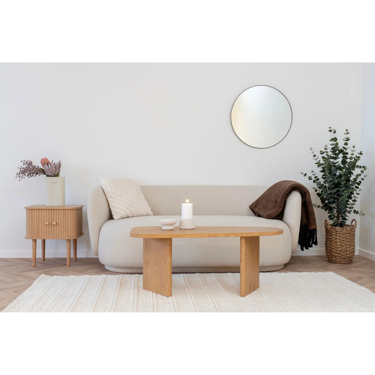 Canapé beige clair capitonné avec accoudoir rond, coussin blanc et plaid marron