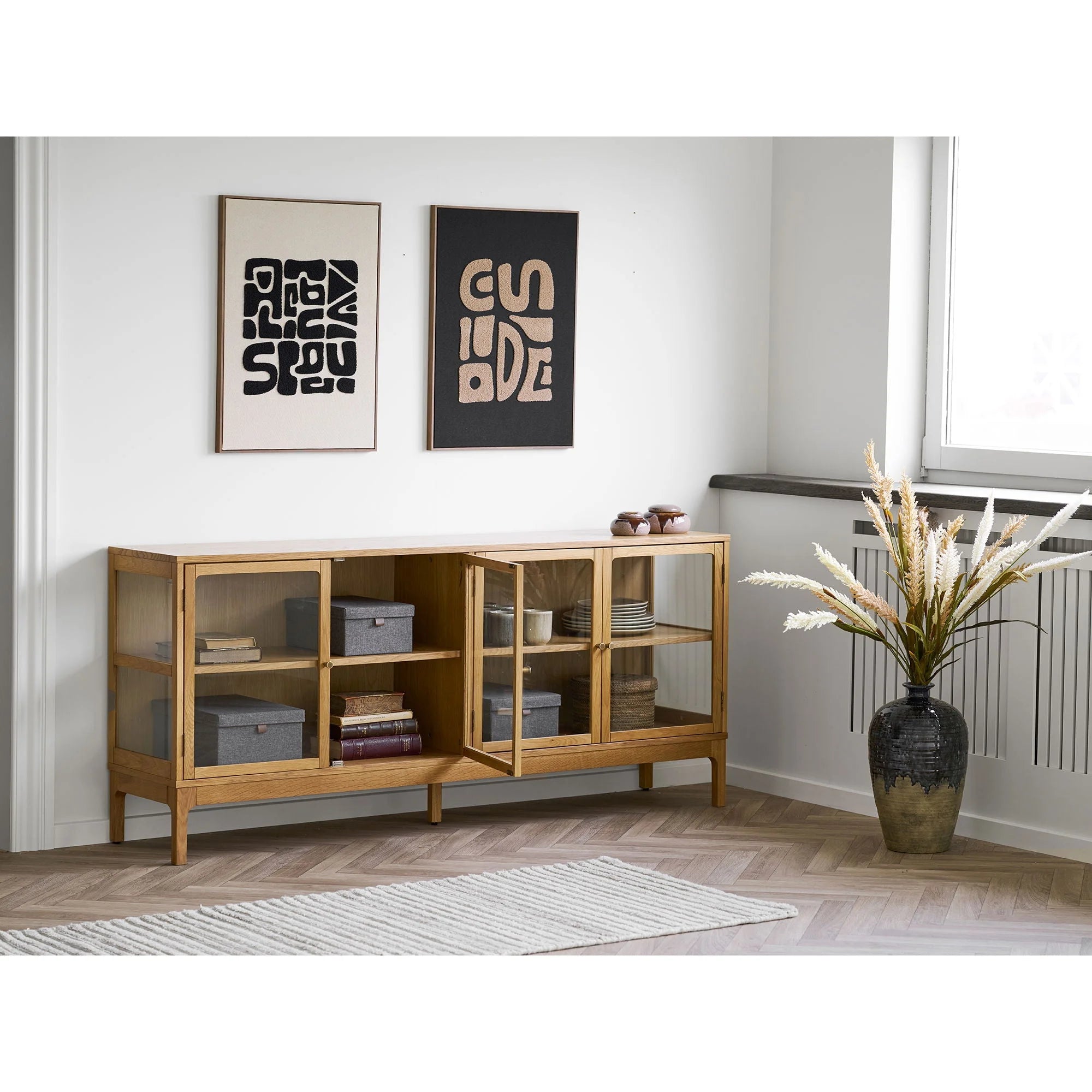 Buffet en bois clair avec portes vitrées et étagères ouvertes, affichant boîtes et objets décoratifs