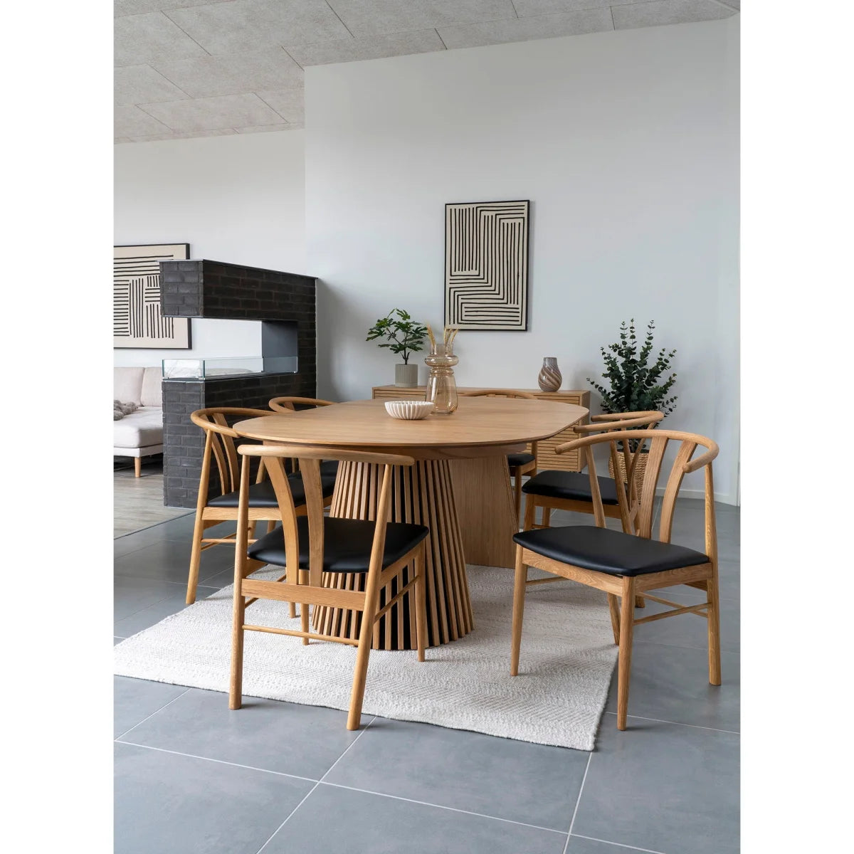 Table à manger en bois clair avec base festonnée et chaises rembourrées noires